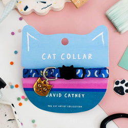 A blue cat collar with a black cat silhouette and a gold cat-shaped tag, displayed on a blue and pink cat-shaped card labelled 'CAT COLLAR' and 'DAVID CATNEY'