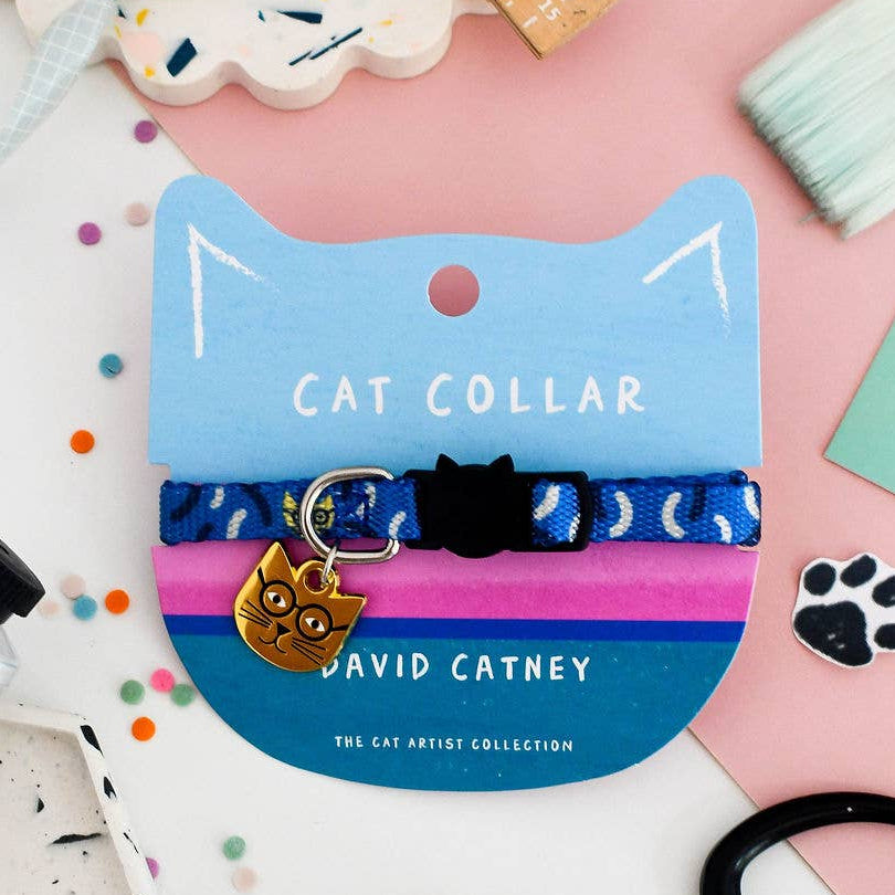A blue cat collar with a black cat silhouette and a gold cat-shaped tag, displayed on a blue and pink cat-shaped card labelled 'CAT COLLAR' and 'DAVID CATNEY'