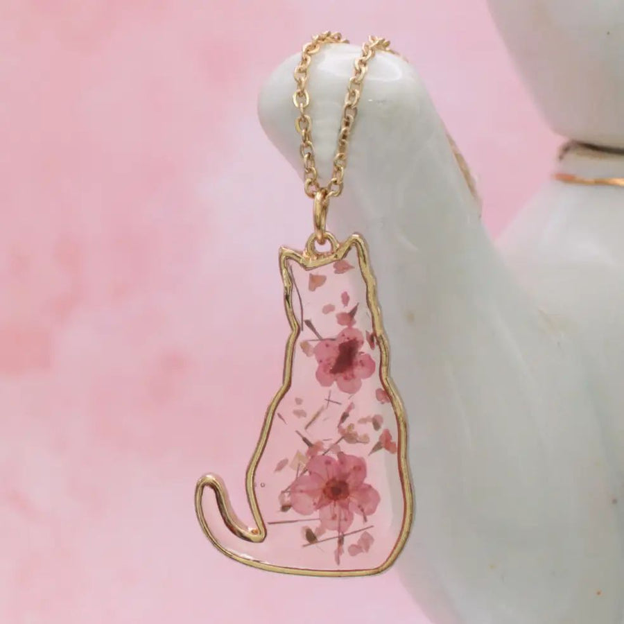 A gold-coloured cat-shaped pendant necklace with pink dried flowers inside the outline