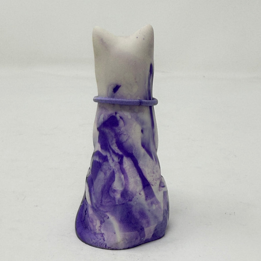 A lavender and white and marbled cat figurine wearing a purple collar with a green heart charm. Rear view.