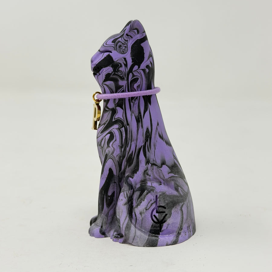 A purple and black marbled cat figurine wearing a purple collar with a gold initial 'P' charm, set against a plain light grey background. Side view.