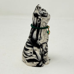 A marbled black and white Lucky Cat figurine wearing a green collar with a green heart charm. Side view.