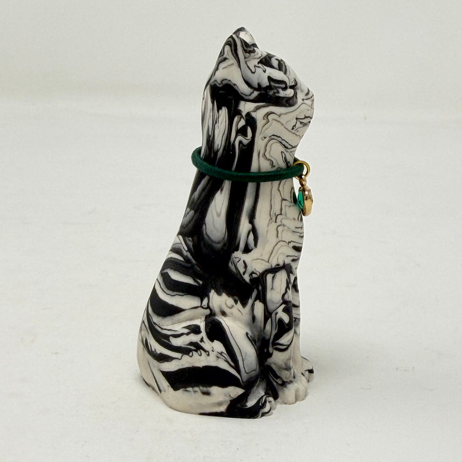 A marbled black and white Lucky Cat figurine wearing a green collar with a green heart charm. Side view.