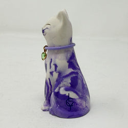 A lavender and white and marbled cat figurine wearing a purple collar with a green heart charm. Side view.