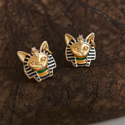 Gold cat-shaped earrings with blue and green accents on a textured brown surface