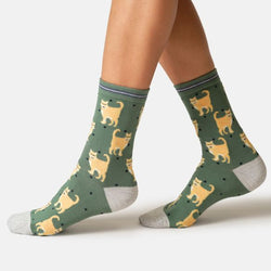 A pair of crew socks worn on a person's feet, featuring a green background with a pattern of yellow walking cats and small black dots