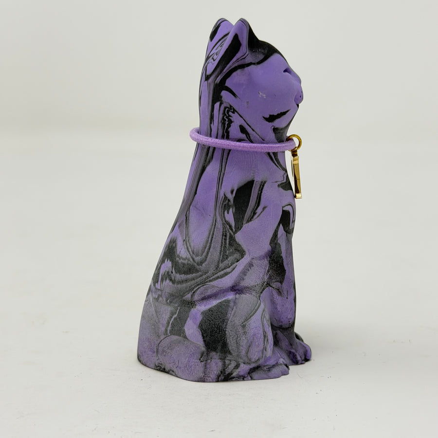A purple and black marbled cat figurine wearing a purple collar with a gold initial 'P' charm, set against a plain light grey background. Side view.