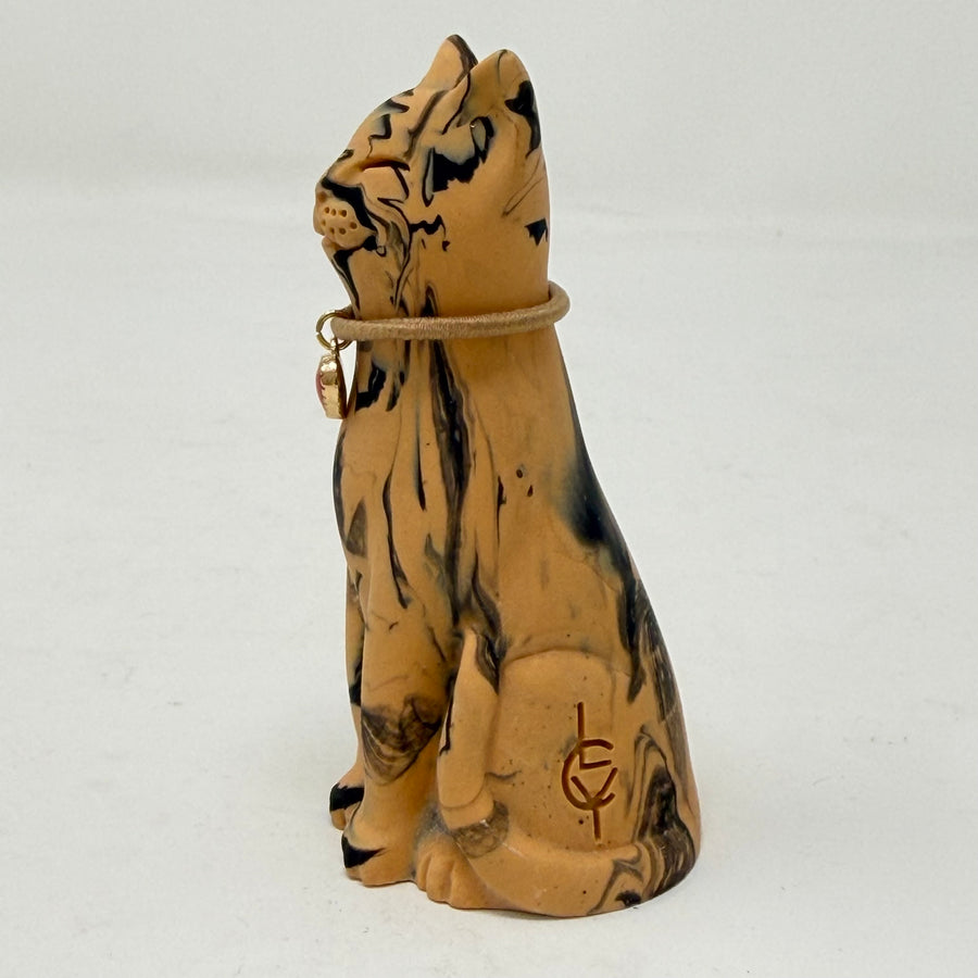 A resin cat figurine with a tan and black marbled pattern, wearing a brown collar with a red heart-shaped charm, set against a plain white background. Side View.