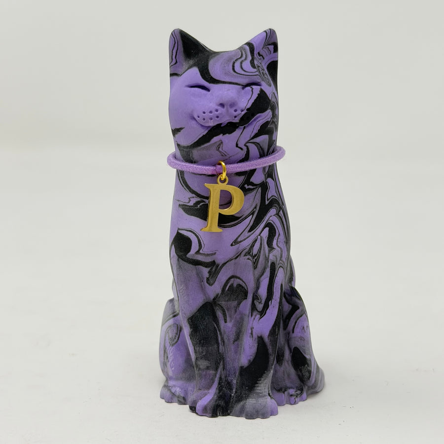 A purple and black marbled cat figurine wearing a purple collar with a gold initial 'P' charm, set against a plain light grey background. Front view