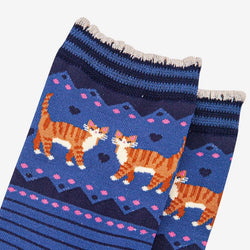 A close-up of a pair of knitted socks featuring a pattern of orange and white striped cats on a blue background with pink hearts