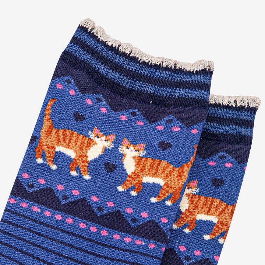 A close-up of a pair of knitted socks featuring a pattern of orange and white striped cats on a blue background with pink hearts