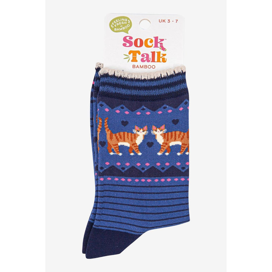 A pair of packaged bamboo crew socks with a blue background, featuring a pattern of two orange-and-white cats, pink hearts, and geometric borders. 