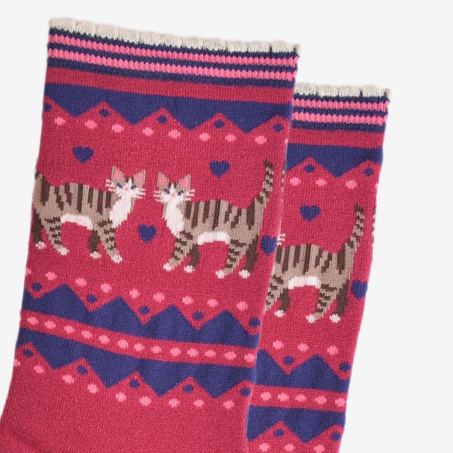 A pair of crew socks with a pink and navy blue Fair Isle pattern featuring two tabby cats and hearts, shown on a plain white background.