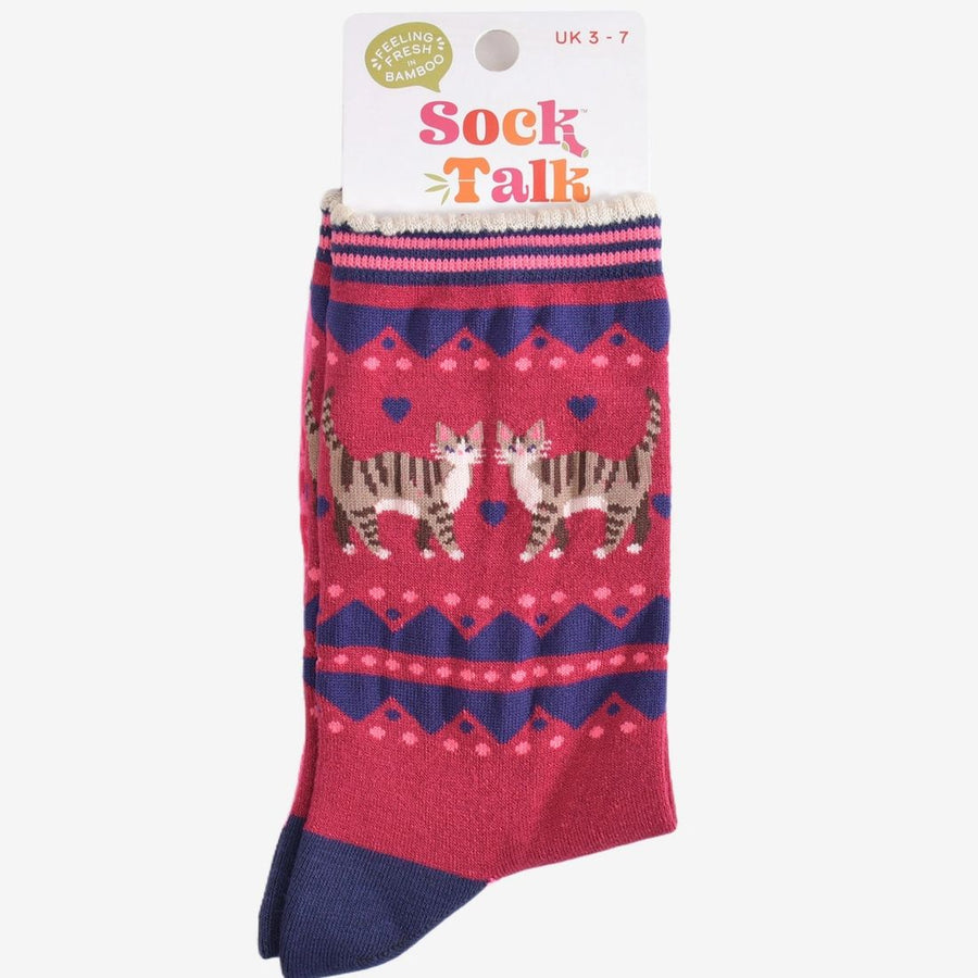 A packaged pair of socks in pinky red with navy blue geometric borders, featuring two tabby cats and small blue hearts in the centre