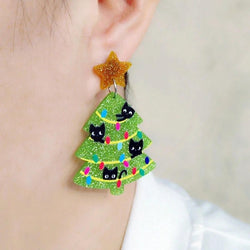 Earrings shaped like Christmas trees with black cats and colourful lights, worn on an ear