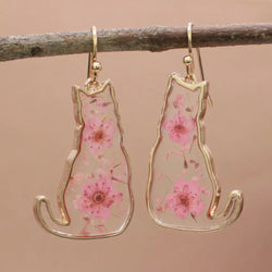 A pair of gold-coloured cat-shaped earrings with pink dried flowers embedded inside