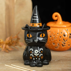 Black cat figurine with a witch hat on a wooden surface with a pumpkin in the background.