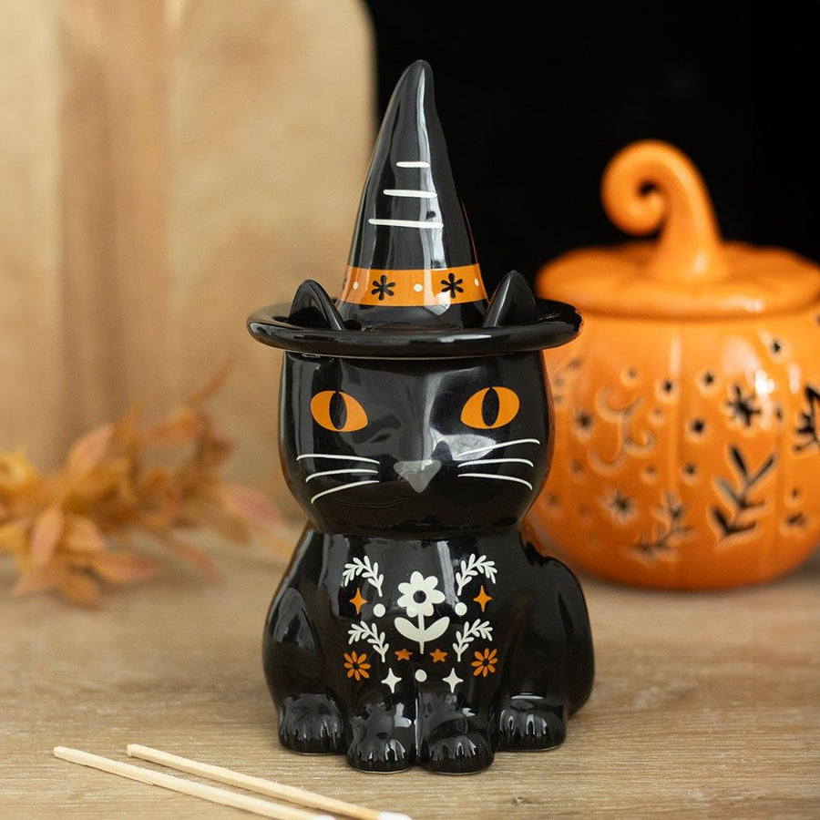 Black cat figurine with a witch hat on a wooden surface with a pumpkin in the background.