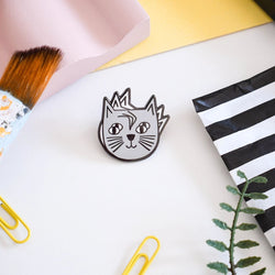 An enamel pin badge with an illustration of a whimsical cat's head