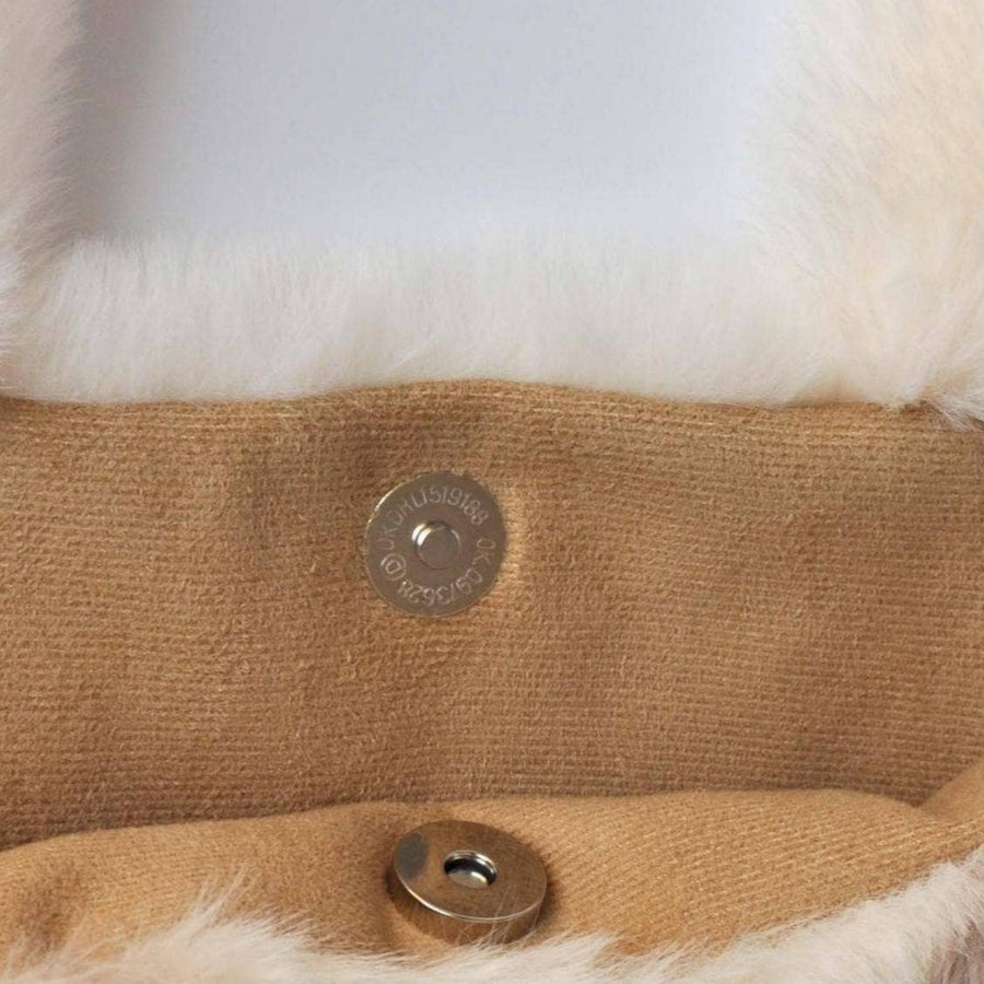 Close-up of a tan knit fabric item with white faux-fur trim and two metal snap buttons