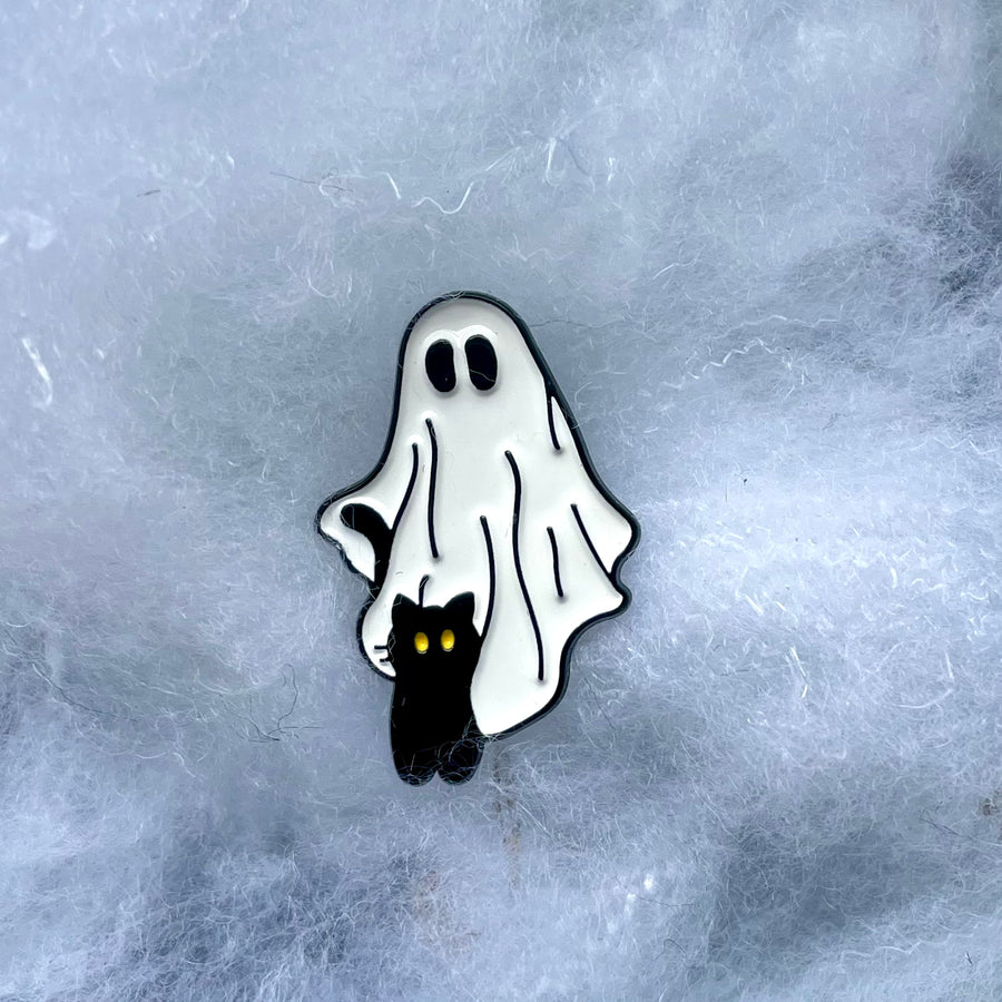 A pin badge featuring a black cat and white ghost on a blue textured background.