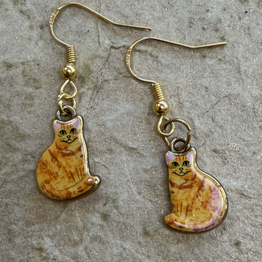 A pair of gold-tone dangle earrings featuring small enamel cat charms with orange tabby fur and green eyes