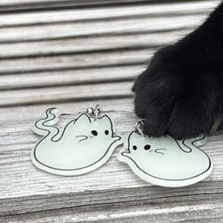 Glowing ghost-shaped earrings on a wooden surface with a cat's paw interacting with them