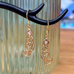 A pair of gold cat earrings with heart-shaped crystals, displayed on a black branch-like stand