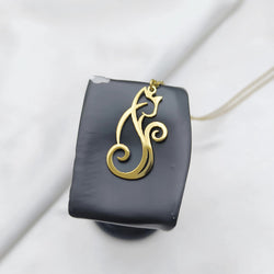 A gold cat-shaped pendant necklace displayed on a black rectangular stand against a soft white fabric background