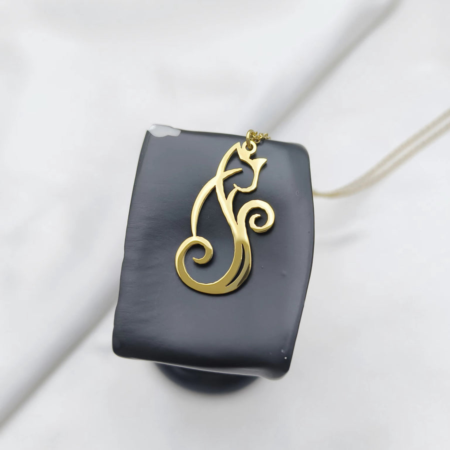 A gold cat-shaped pendant necklace displayed on a black rectangular stand against a soft white fabric background