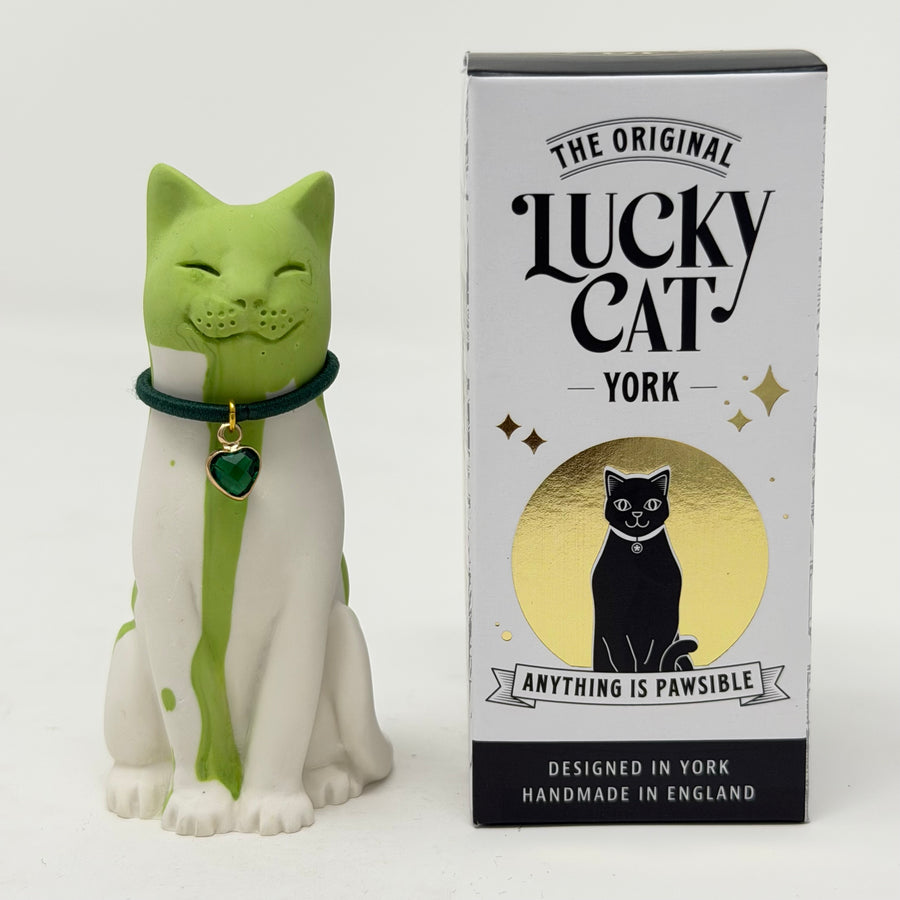 A resin Lucky Cat figurine in green and white next to its branded bos "The Original Lucky Cat York". The cat has a green head and back, a white body, and a dark green collar with a gold heart charm.