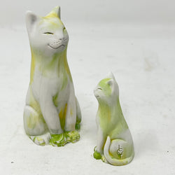 Two marbled smiling lucky cat figures in shades of yellow, green and white on a light grey background