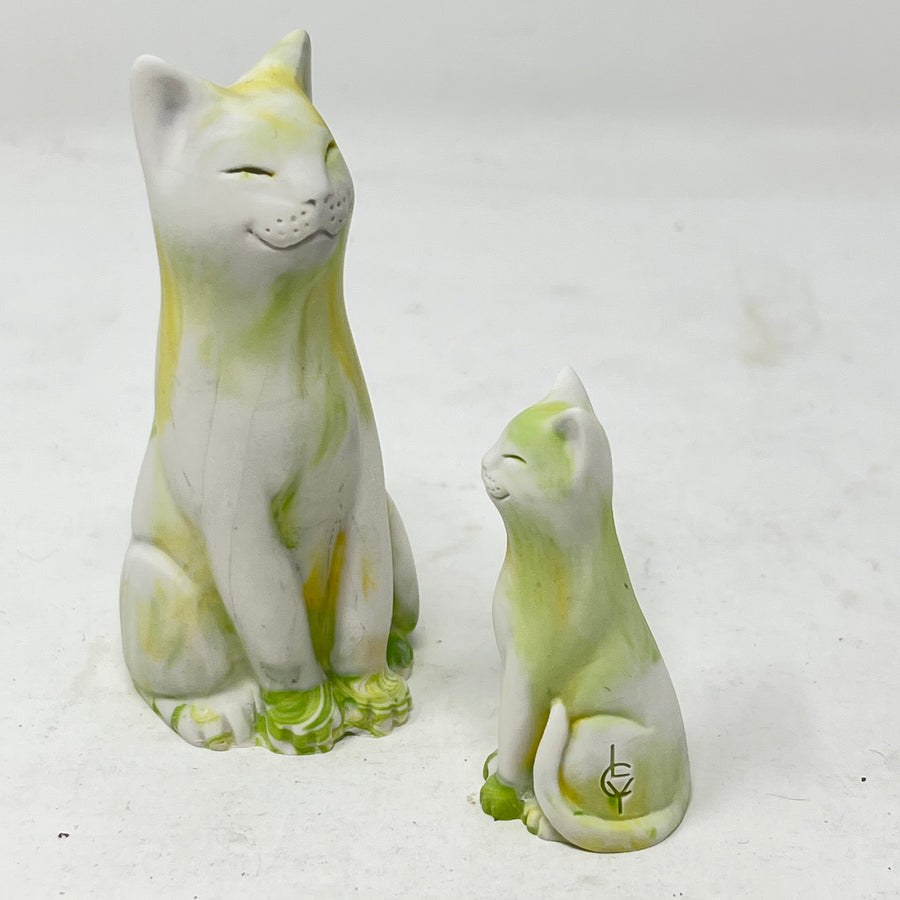 Two marbled smiling lucky cat figures in shades of yellow, green and white on a light grey background