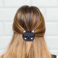 Person with long blonde hair wearing a black cat-shaped hair clip against a white tiled wall.