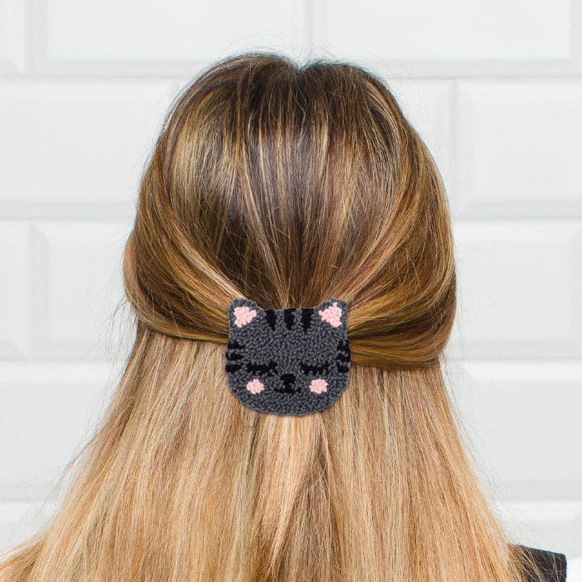 Person with long blonde hair wearing a black cat-shaped hair clip against a white tiled wall.