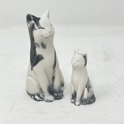 Two marbled smiling lucky cat figures in shades of grey and white on a light grey background
