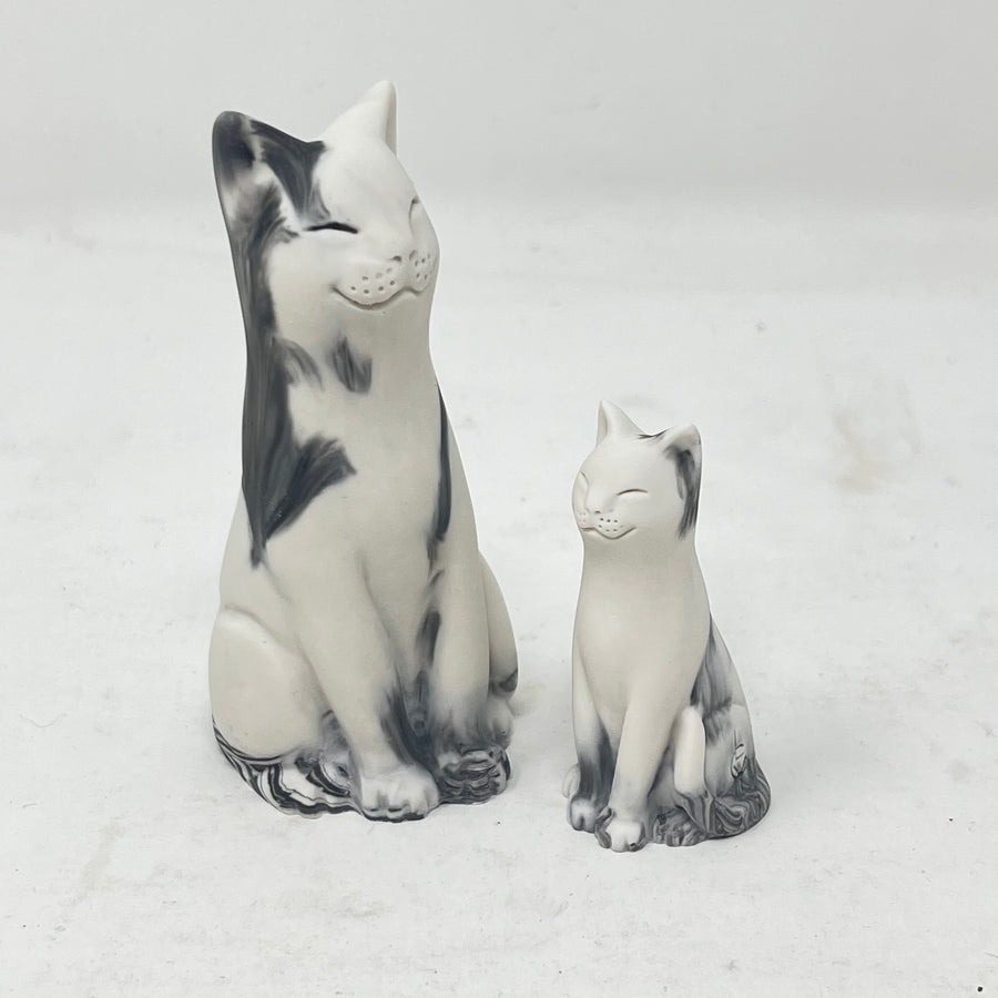 Two marbled smiling lucky cat figures in shades of grey and white on a light grey background