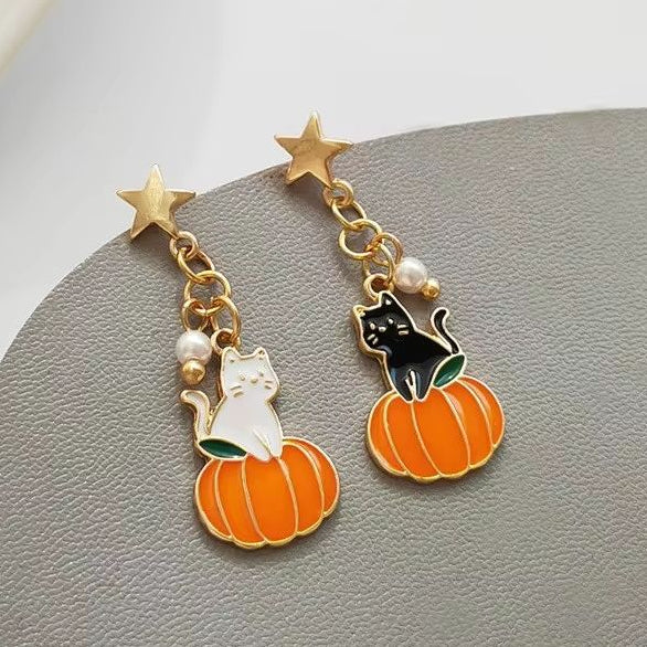 A pair of gold-tone dangle earrings with charms shaped like a white cat on an orange pumpkin and a black cat on a pumpkin