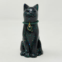A glossy black lucky cat figurine with blue and green holographic speckles, wearing a dark green collar with a gold heart-shaped charm