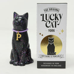 A black glittery cat figurine wearing a purple collar with a gold letter P, shown next to its white and gold retail box labeled 'The Original Lucky Cat York'.