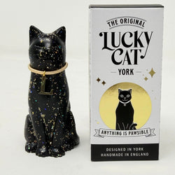 A black glittery lucky cat figurine wearing a gold collar with a letter L charm, sitting next to its branded box 'The Original Lucky Cat York'.