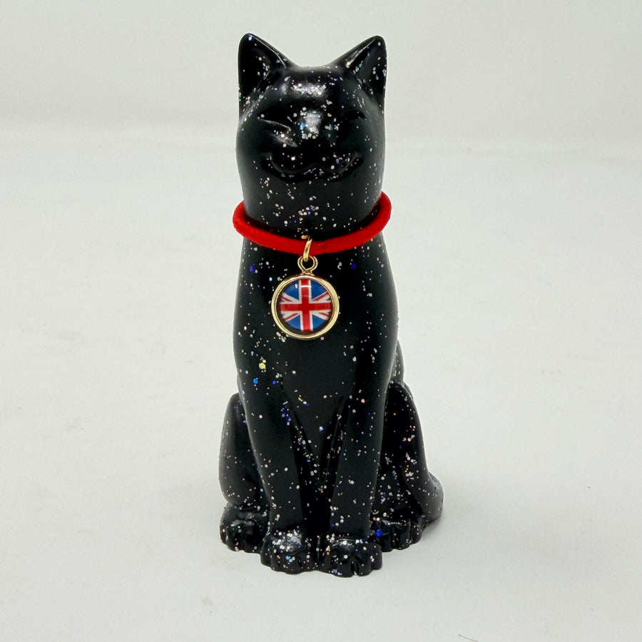 A glossy black lucky cat figurine with silver holographic speckles, wearing a bright red collar with a round pendant featuring the Union Jack flag