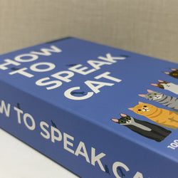 A close-up of a blue box titled "How to Speak Cat" with white lettering and cartoon cat illustrations on the cover