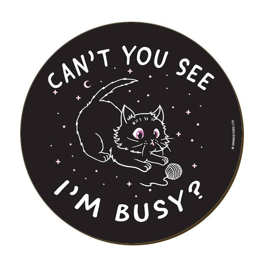 A round black coaster with a white line-art illustration of a cat playing with a ball of yarn, surrounded by the text 'CAN'T YOU SEE I'M BUSY?'