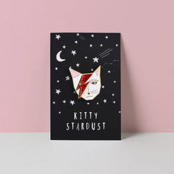 White Cat head wiht Ziggy Stardust style lightning flash across face. The whole forming an enamel pin on a Kitty Stardust branded backing card