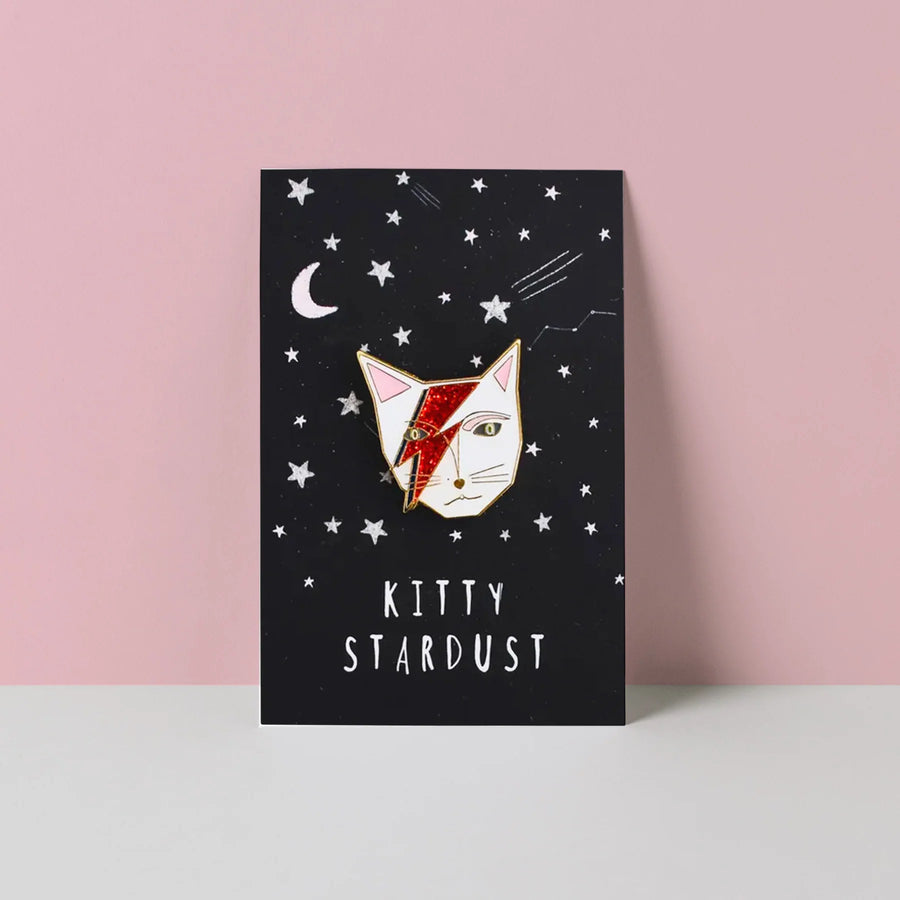 White Cat head wiht Ziggy Stardust style lightning flash across face. The whole forming an enamel pin on a Kitty Stardust branded backing card