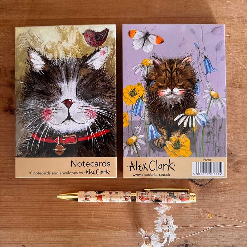 Two illustrated notecard boxes by Alex Clark, one with a black-and-white cat and one with a tabby cat among flowers and butterflies