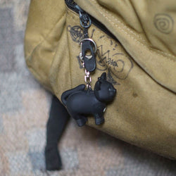 Black cat-shaped keychain attached to a beige bag with visible branding.