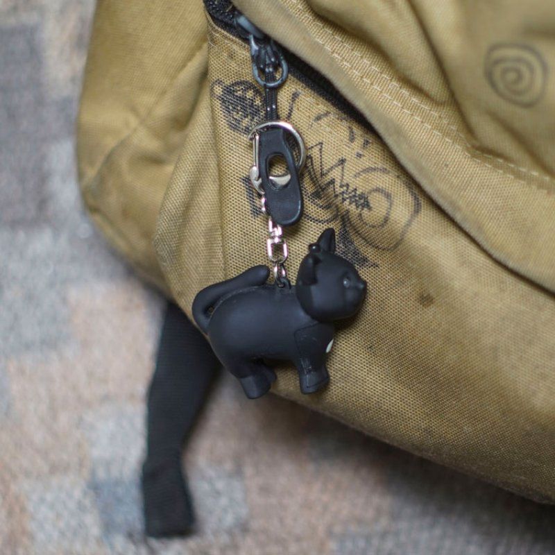 Black cat-shaped keychain attached to a beige bag with visible branding.