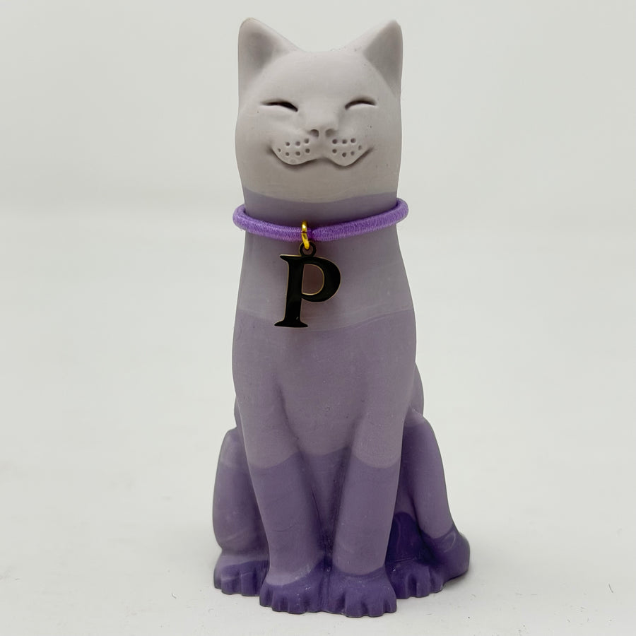A lavender lucky cat figurine,with a lavender collar and a gold letter P charm